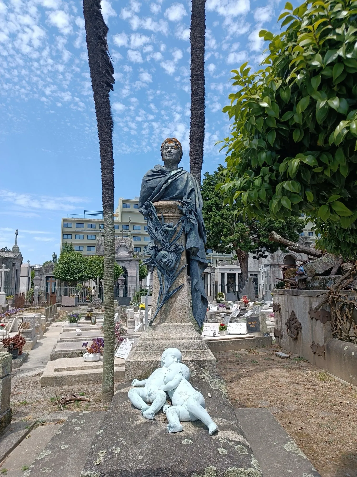 Uma figura drapejada de luto sobre um jazigo, com querubins de mármore aos seus pés.