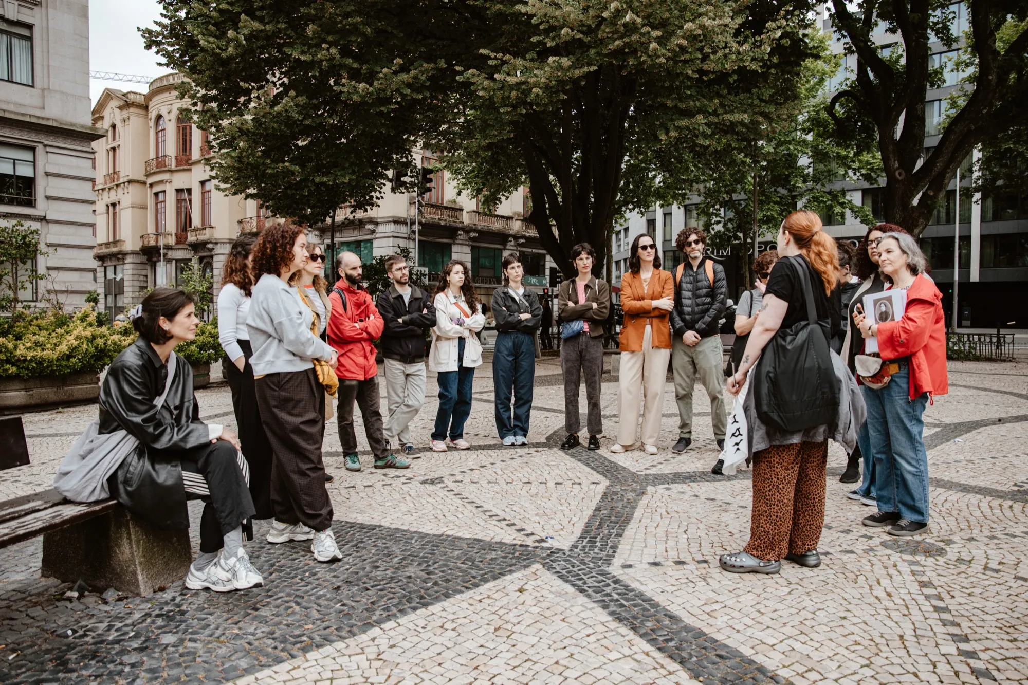 Grupo do passeio em roda, numa praça com calçada portuguesa.